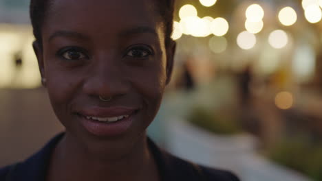 Nahaufnahme-Porträt-Einer-Schönen-Afroamerikanischen-Geschäftsfrau,-Die-In-Die-Kamera-Blickt-Und-Selbstbewusst-Lächelt-Und-Einen-Nasenring-Im-Abendlichen-Stadthintergrund-Mit-Hellem-Bokeh-Trägt