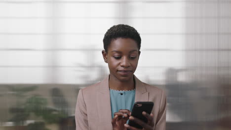 portrait-of-professional-african-american-business-woman-smiling-enjoying-texting-browsing-using-smartphone-in-office-workpace