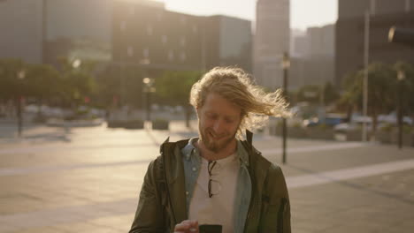 portrait-of-handsome-bearded-hipster-man-texting-browsing-using-smartphone-mobile-app-smiling-in-windy-urban-city-at-sunset