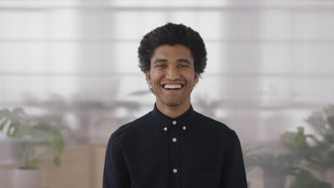 portrait-of-young-mixed-race-man-laughing-cheerful-looking-at-camera-enjoying-successful-job-opportunity-ambitious-male-in-office-workspace-background