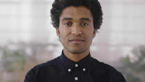close-up-portrait-of-young-confident-mixed-race-man-looking-at-camera-smiling-proud-in-office-workspace-background