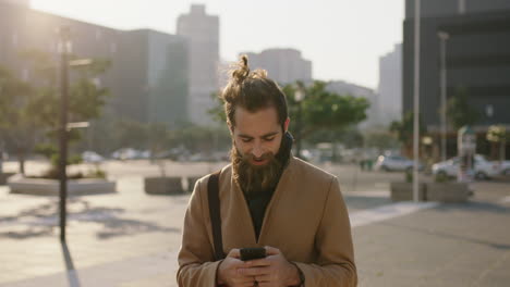portrait-of-attractive-stylish-young-bearded-hipster-man-texting-browsing-using-smartphone-messaging-app-in-city