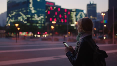 portrait-of-young-blonde-woman-texting-browsing-using-smartphone-social-media-app-in-urban-city-at-night-enjoying-lights