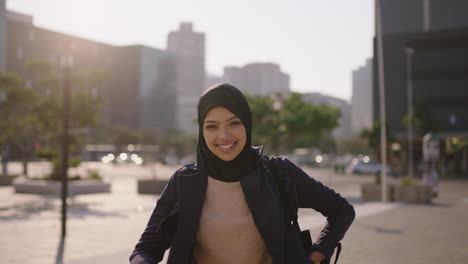 Porträt-Einer-Jungen-Glücklichen-Muslimischen-Geschäftsfrau,-Die-Lächelnd-In-Die-Kamera-Blickt-Und-Selbstbewusst-Ein-Hadschib-Kopftuch-In-Einer-Windigen-Stadt-Trägt