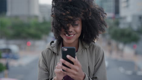 Porträt-Einer-Glücklichen-Afroamerikanischen-Frau,-Die-In-Der-Stadt-Smartphone-SMS-Nutzt-Und-Lächelt-Und-Das-Surfen-Von-Online-Nachrichten-Auf-Dem-Mobiltelefon-Genießt.-Wind-Weht-Afro-Frisur