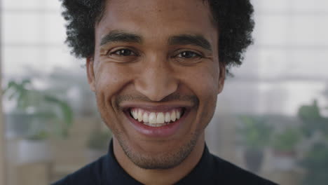 close-up-portrait-of-young-mixed-race-man-smiling-cheerful-looking-at-camera-enjoying-successful-job-opportunity-ambitious-male-in-office-workspace-background