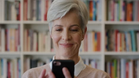 Porträt-Einer-Schönen-älteren-Geschäftsfrau,-Die-Ihr-Smartphone-Nutzt-Und-Das-Surfen-Im-Internet-Beim-SMS-Schreiben-Genießt-Und-Lustige-Nachrichten-Liest,-Die-Glücklich-Im-Bücherregal-Hintergrund-Lächeln