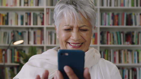 portrait-of-friendly-indian-middle-aged--teacher-laughing-standing-in-library-using-smartphone