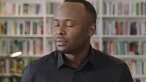 Porträt-Eines-Jungen-Afroamerikanischen-Mannes,-Der-Den-Kopf-Dreht-Und-In-Die-Kamera-Blickt,-Die-In-Der-Bibliothek-Steht