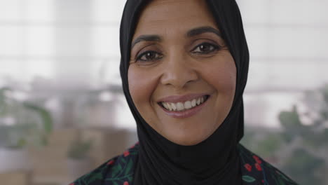 close-up-portrait-of-senior-muslim-business-woman-smiling-looking-cheerful-at-camera-wearing-traditional-headscarf-mature-experienced-female-in-office-workspace