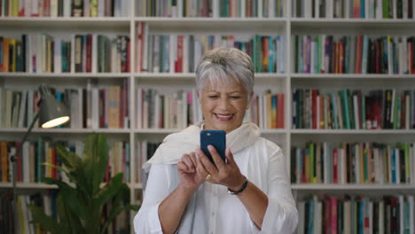 portrait-of-friendly-indian-middle-aged--teacher-laughing-standing-in-library-using-smartphone