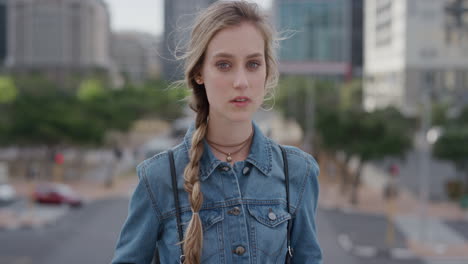 portrait-young-attractive-blonde-woman-student-in-city-looking-confident-at-camera-wearing-denim-jacket-urban-cityscape-background-wind-blowing-hair