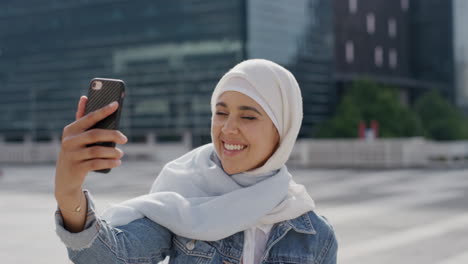Porträt-Einer-Jungen,-Hübschen-Muslimischen-Frau,-Die-Ihr-Smartphone-Benutzt-Und-Ein-Selfie-Foto-Macht,-Das-In-Der-Stadt-Posiert-Und-Stadtreisen-Genießt,-Indem-Sie-Erfahrungen-Mit-Einem-Hijab-Kopftuch-Und-Einem-Modernen-Lebensstil-Teilt