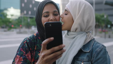 Porträt-Junger-Muslimischer-Frauen,-Die-Posieren,-Tochter-Küsst-Mutter-Auf-Die-Wange-Und-Macht-Ein-Selfie-Foto-Mit-Smartphone-Kameratechnologie-Im-Städtischen-Hintergrund