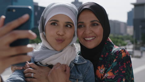 Nahaufnahme-Eines-Porträts-Einer-Muslimischen-Mutter-Und-Tochter,-Die-Fröhlich-Lächelnd-Umarmt-Und-In-Einer-Sonnigen-Stadt-Mit-Dem-Smartphone-Ein-Selfie-Foto-Macht