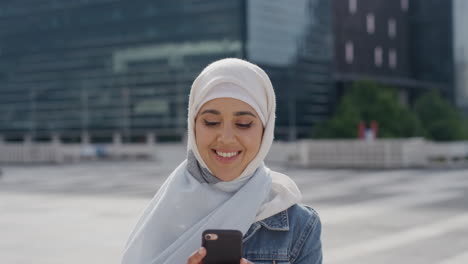 Porträt-Einer-Jungen-Muslimischen-Studentin,-Die-Ihr-Smartphone-In-Der-Stadt-Nutzt-Und-Dabei-Genießt,-SMS-Zu-Schreiben-Und-Nachrichten-Auf-Dem-Mobiltelefon-Zu-Durchsuchen,-Während-Sie-Ein-Hijab-Kopftuch-Trägt,-Sonniger-Städtischer-Hintergrund,-Digitale-Kommunikation
