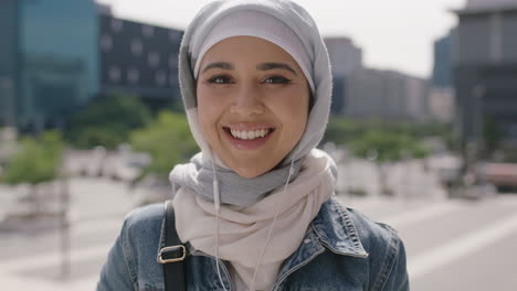 Retrato-De-Una-Hermosa-Joven-Estudiante-Musulmana-Sonriendo-Confiada-Ante-La-Cámara-Escuchando-Música-Usando-Auriculares-Usando-Un-Pañuelo-En-La-Cabeza-Hajib