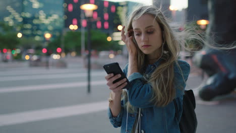 portrait-of-young-beautiful-blonde-woman-wearing-earphones-listening-to-music-smiling-happy-texting-browsing-using-smartphone-enjoying-calm-urban-evening-in-city