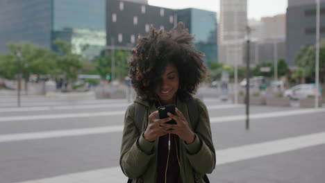 Retrato-De-Una-Hermosa-Y-Moderna-Mujer-Afroamericana-Enviando-Mensajes-De-Texto-Navegando-Usando-Una-Aplicación-De-Redes-Sociales-Para-Teléfonos-Inteligentes-Escuchando-Música-Usando-Auriculares-En-Una-Ciudad-Urbana