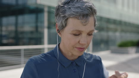 portrait-of-mature-independent-business-woman-listening-to-music-using-earphones-wearing-backpack-in-city