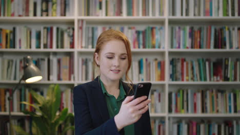 portrait-of-beautiful-young-red-head-business-woman-executive-texting-browsing-using-smartphone-mobile-app-in-library-background