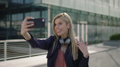 Retrato-De-Una-Joven-Y-Animada-Mujer-De-Negocios-Rubia-En-Prácticas-Sonriendo-Posando-Tomando-Una-Foto-Selfie-Usando-La-Cámara-Del-Teléfono-Inteligente-En-La-Ciudad