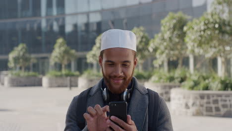 Retrato-Joven-Empresario-Independiente-Usando-Un-Teléfono-Inteligente-En-La-Ciudad-Disfrutando-De-Mensajes-De-Texto-Navegando-En-Línea-Feliz-Hombre-De-Negocios-Musulmán-Usando-Sombrero-Kufi