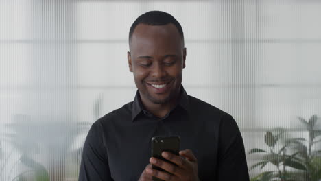 Retrato-Joven-Hombre-De-Negocios-Afroamericano-Usando-Un-Teléfono-Inteligente-En-La-Oficina-Disfrutando-De-Mensajes-De-Texto-Navegando-En-Un-Teléfono-Móvil-Enviando-Sms-Correo-Electrónico-Sonriendo-Feliz-Satisfacción-En-Cámara-Lenta
