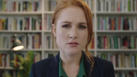 portrait-of-beautiful-young-red-head-business-woman-intern-looking-serious-pensive-at-camera-in-library-bookshelf-background