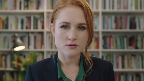 portrait-of-attractive-young-red-head-business-woman-intern-turns-head-looking-pensive-serious-at-camera-in-library-study-background