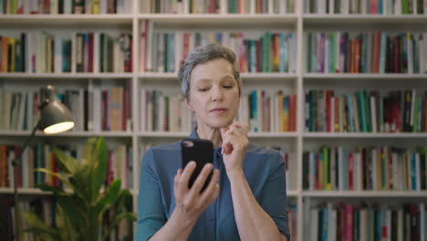 portrait-of-mature-caucasian-woman-looking-pensive-thinking-texting-browsing-using-smartphone-mobile-technology-in-library