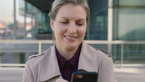 Retrato-De-Una-Mujer-De-Negocios-Senior-Sonriendo-Feliz-Disfrutando-Usando-Mensajes-De-Texto-De-Teléfonos-Inteligentes-Navegando-Por-Mensajes-De-Redes-Sociales-En-El-Fondo-Urbano