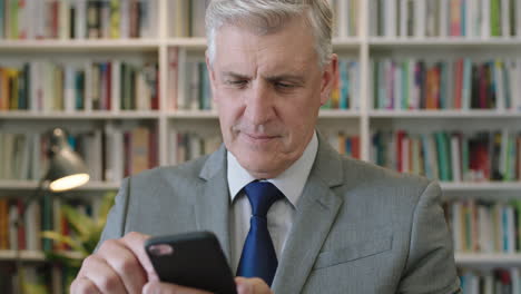 portrait-of-pensive-caucasian-businessman-boss-texting-browsing-using-smartphone-networking-app-brainstorming-ideas-in-library-bookshelf-background