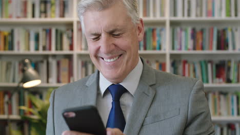 portrait-of-mature-caucasian-businessman-boss-laughing-cheerful-reading-funny-text-messages-using-smartphone-mobile-technology-in-office-study-library