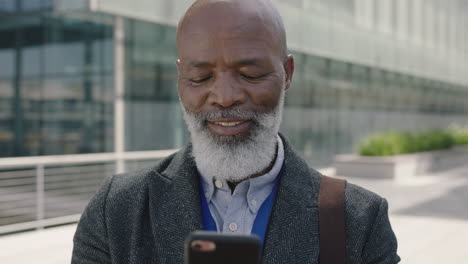 Nahaufnahme-Eines-Porträts-Eines-älteren-Afroamerikanischen-Geschäftsmannes,-Der-Glücklich-Lächelt-Und-Sein-Smartphone-Benutzt,-Um-Nachrichten-Zu-überprüfen-Und-SMS-Im-Städtischen-Hintergrund-Zu-Schreiben