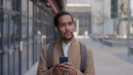 portrait-attractive-young-hispanic-businessman-using-smartphone-in-city-browsing-online-messages-texting-on-mobile-phone-slow-motion-urban-commuter