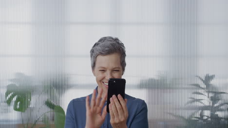 portrait-happy-senior-business-woman-using-smartphone-video-chatting-waving-hand-blow-kiss-enjoying-communication-on-mobile-phone-in-office-slow-motion