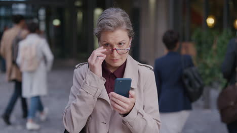 portrait-successful-mature-caucasian-woman-using-smartphone-in-city-enjoying-texting-browsing-online-messages-on-mobile-phone-wearing-glasses-slow-motion
