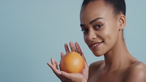 portrait-attractive-young-african-american-woman-holding-grapefruit-smiling-enjoying-natural-healthy-skincare-essence-beautiful-female-with-perfect-complexion-on-blue-background
