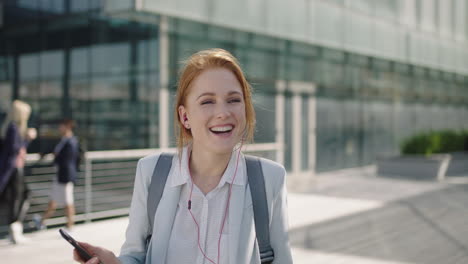portrait-of-cheerful-red-head-business-woman-executive-wearing-earphones-listening-to-music-texting-browsing-using-smartphone-social-media-app-laughing-reading-messages