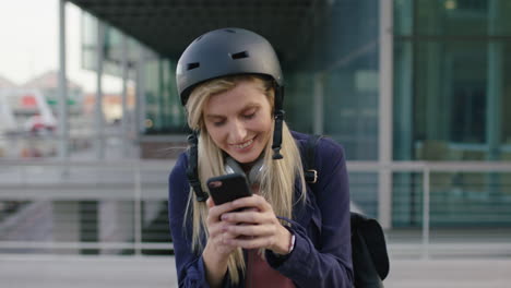 portrait-of-young-cute-blonde-business-woman-intern-wearing-helmet-texting-browsing-social-media-using-smartphone-in-city