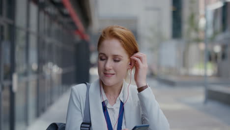 portrait-happy-young-red-head-business-woman-using-smartphone-texting-sending-messages-enjoying-listening-to-music-wearing-earphones-in-relaxed-urban-city-slow-motion