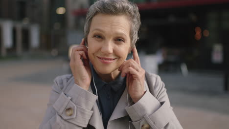 portrait-of-mature-business-woman-smiling-happy-puts-on-earphones-listening-to-music-enjoying-leaving-work-urban-commuting