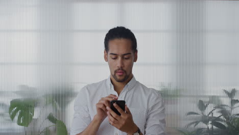 portrait-pensive-young-hispanic-businessman-using-smartphone-in-office-browsing-messages-working-sending-emails-on-mobile-phone-texting-slow-motion-digital-communication