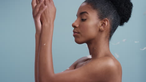 slow-motion-beauty-portrait-attractive-african-american-woman-feathers-falling-on-smooth-skin-touching-bare-shoulders-enjoying-natural-skincare-gently-caressing-body-in-blue-background