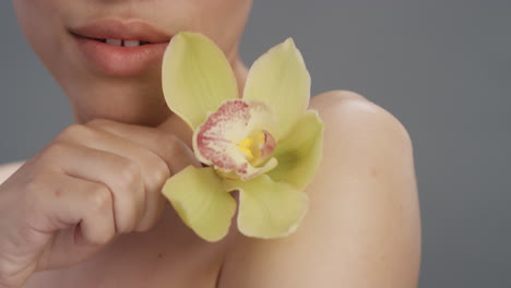 close-up-portrait-beauty-woman-touching-skin-with-orchid-flower-caressing-smooth-healthy-complexion-enjoying-natural-sensual-fragrance-flirtatious-young-female-on-grey-background-skincare-concept