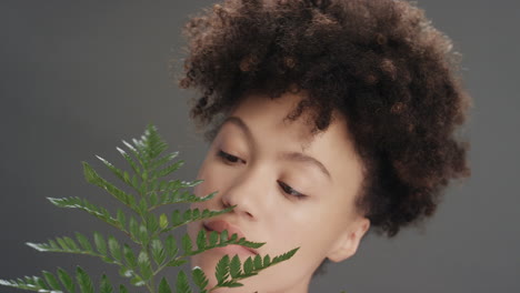 close-up-portrait-beautiful-mixed-race-woman-touching-face-with-fern-leaf-caressing-smooth-healthy-skin-complexion-enjoying-playful-natural-beauty-on-grey-background-skincare-concept