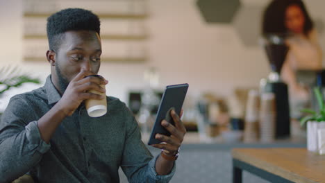 Afroamerikanischer-Geschäftsmann-Benutzt-Tablet-Computer-Im-Café,-Trinkt-Kaffee-Und-Schaut-Sich-Online-Unterhaltung-An.-Stilvoller-Unternehmer-Liest-Social-Media-Nachrichten-Und-Genießt-Die-Internetverbindung