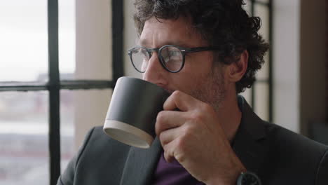 portrait-happy-mature-business-man-drinking-coffee-at-home-enjoying-relaxed-morning-looking-out-window-planning-ahead-thinking-successful-caucasian-male-smiling-wearing-glasses-in-apartment-loft