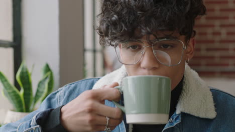 stylish-young-hispanic-man-student-drinking-coffee-at-home-looking-out-window-thinking-planning-ahead-enjoying-relaxing-lifestyle-wearing-trendy-fashion-glasses